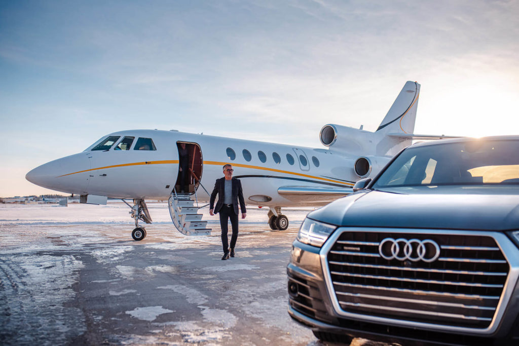 Business man walks from chartered aircraft to personal vehicle parked on the runway.