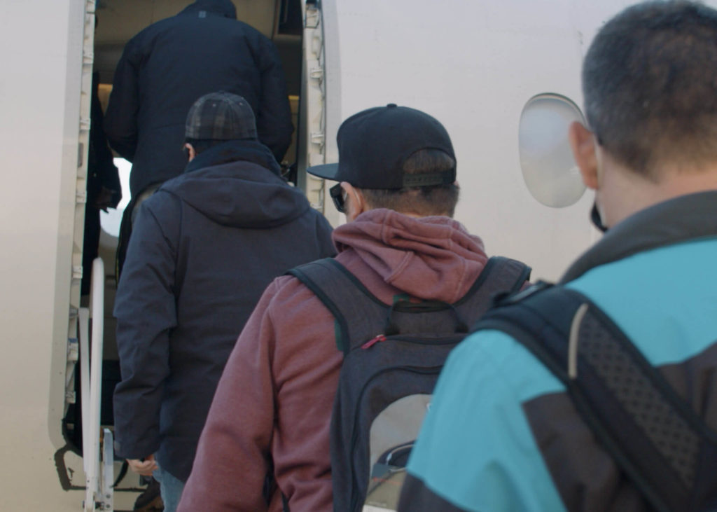 Crew wearing backpacks and face masks line up to board Genesis Aviation charter flight