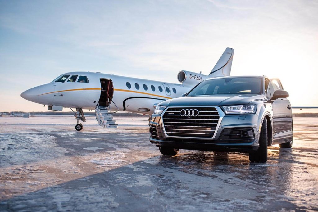 Shiny Audii sedan is parked on the tarmac right beside a Genesis Aviation charter plane.
