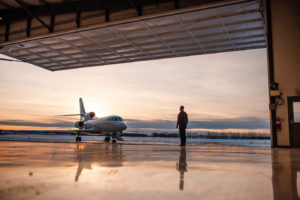Man in suit stands on the tarmac in front of Genesis Aviation private plane as the sun sets